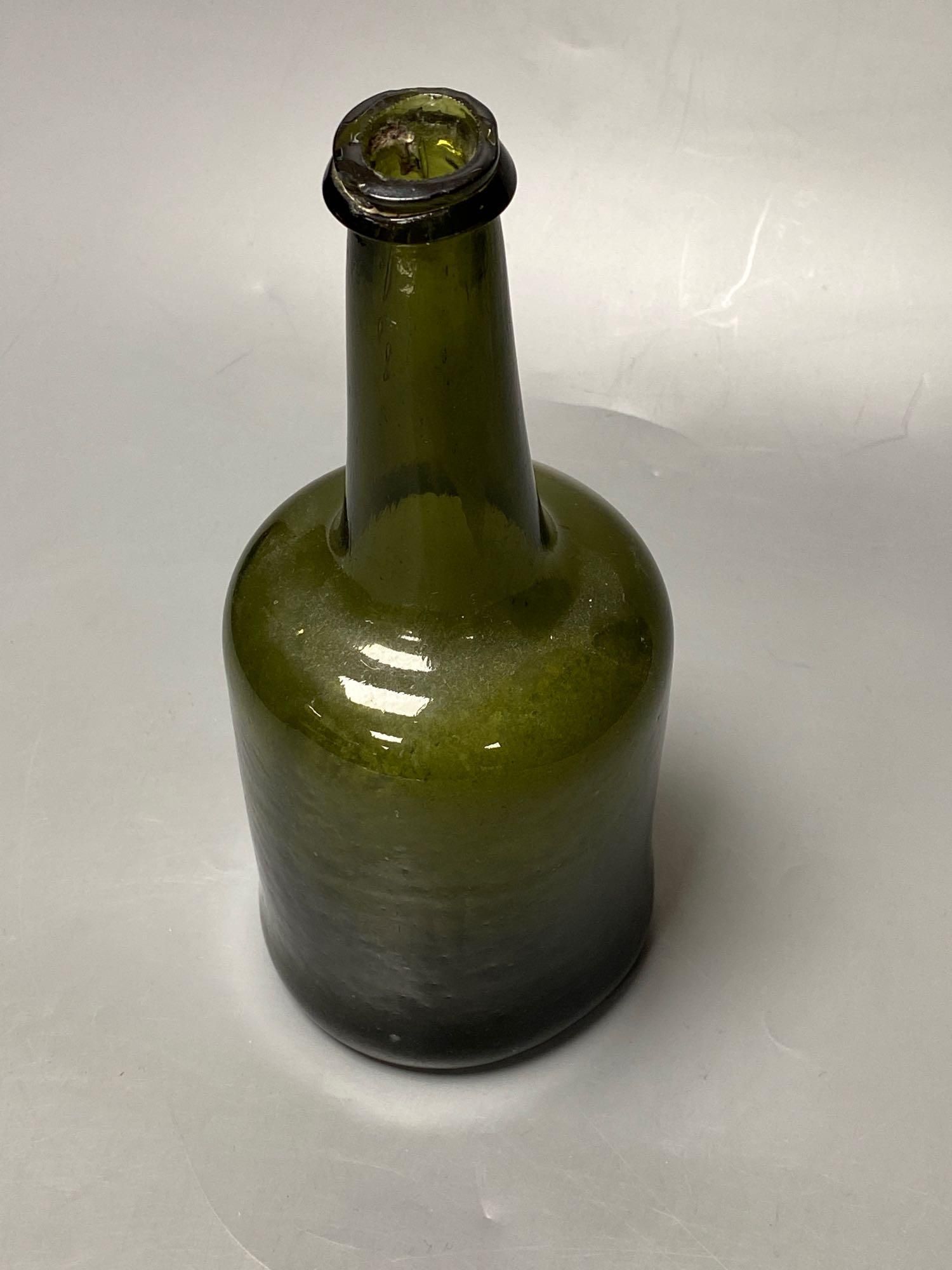 An early 18th century dark green glass wine bottle with a kick in based, 23cm